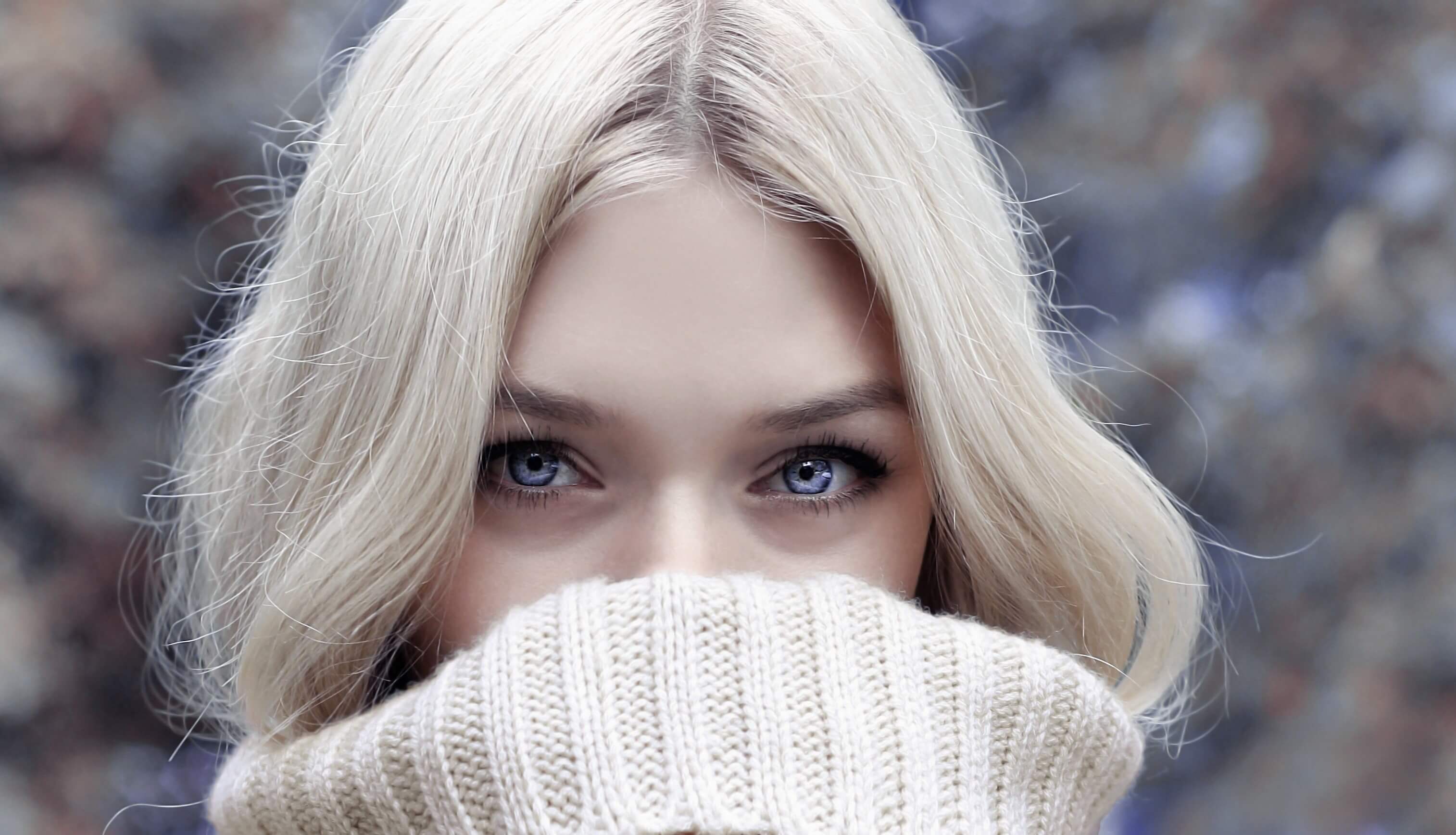 blonde woman with beautiful blue eyes hiding face in white sweater