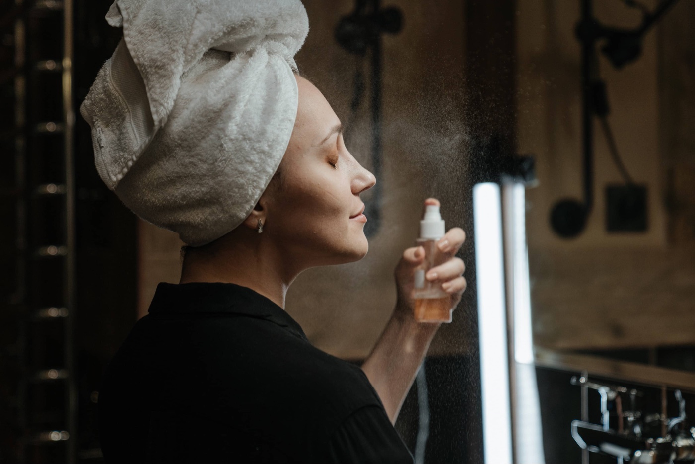 woman in robe setting makeup with facial spray