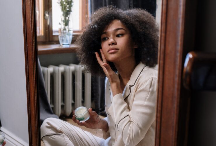 young woman sitting on the floor applying skincare in a mirror
