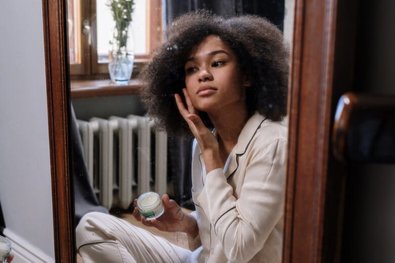 young woman sitting on the floor applying skincare in a mirror