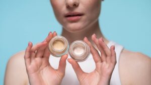 close up of woman holding two glass jars of light makeup