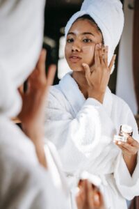 woman in a robe and towel applying skincare